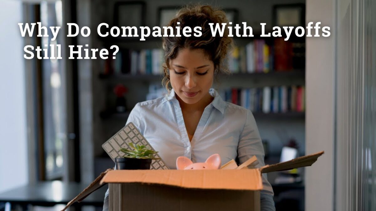Woman standing in an office looking down at a box of her belongings after being laid off, illustrating the question “Why do companies with layoffs still hire?”